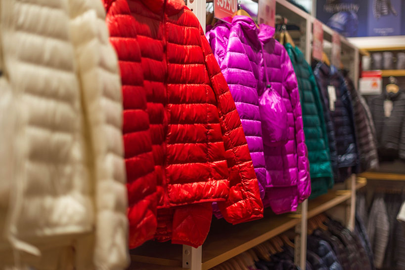 Different coloured puffy jackets hang on store shelves. 