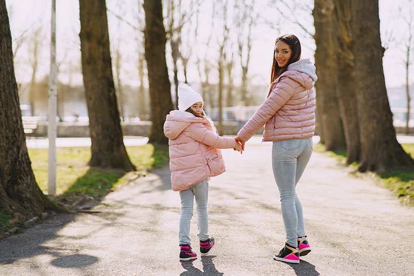 Mother and daughter wear spring jackets while walking in a park